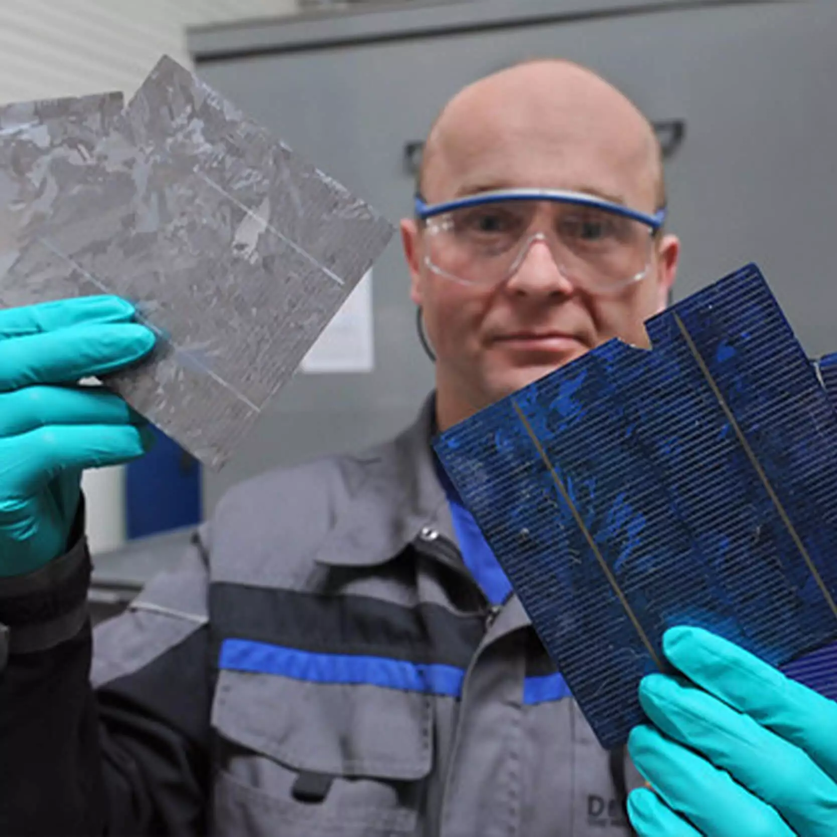 Bald, white, male with safety glasses and turquoise gloves holidng solar panel scraps