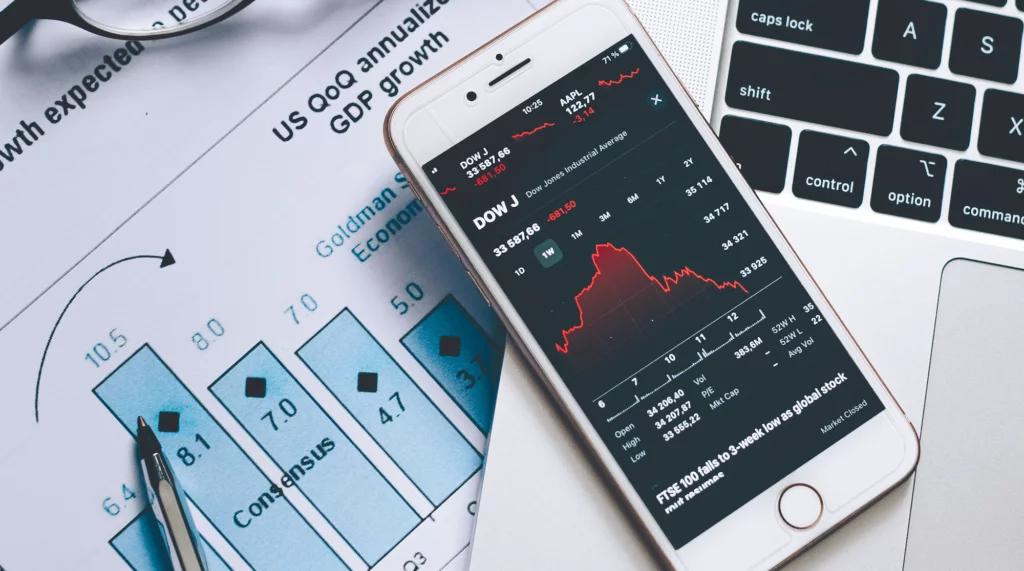 Stock Market and GDP Growth Stock market trends and patterns on iPhone sitting on a laptop with GDP growth chart behind