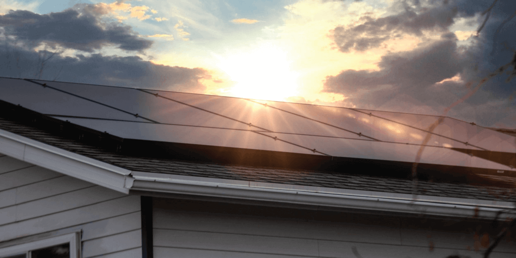 Solar panel system installed on roof with the sun shining brightly through darker clouds