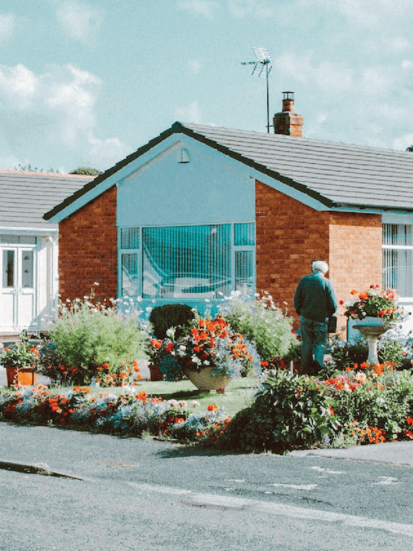 Male watering flowers outside of an orange, red brick, free-standing, single-level home