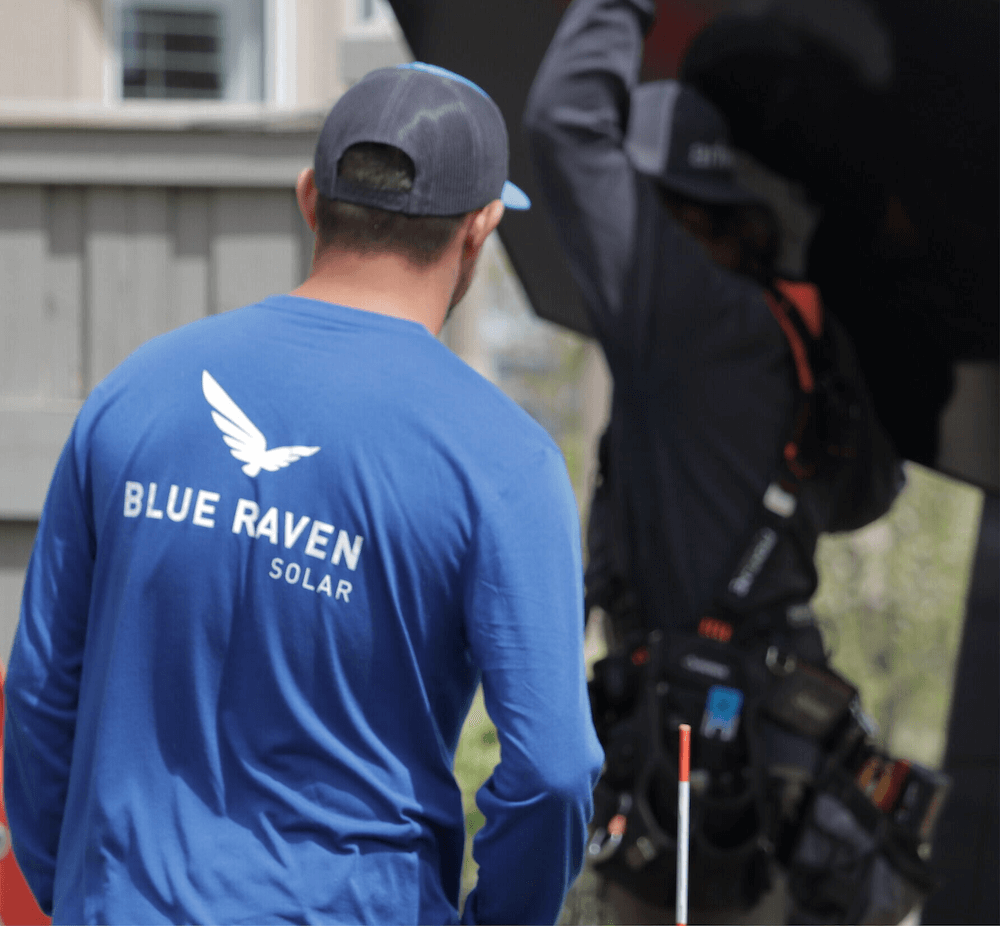 Blue Raven Solar Installer_Blue Shirt Blue Raven Solar installer in a blue branded, long-sleeve t-shirt approaching another install crew member