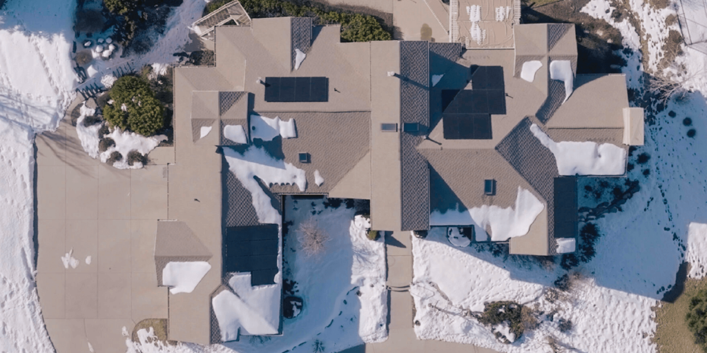 Aerial view of a large house with multiple PV panels installed and snow intermixed
