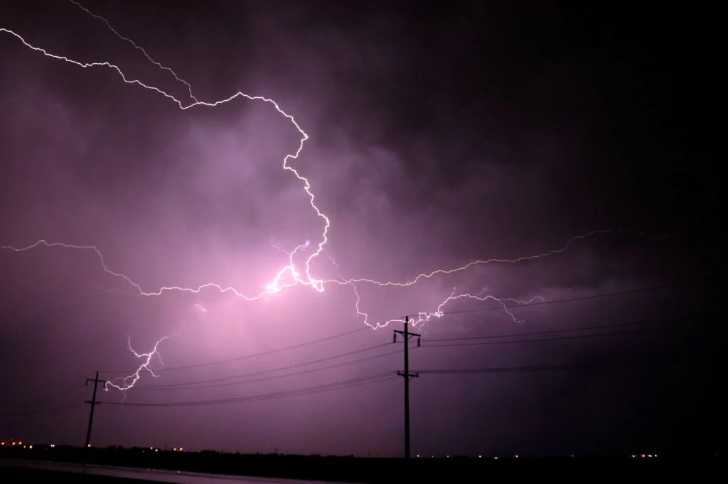 Lightening at night, lighting up the sky with power lines in the foreground