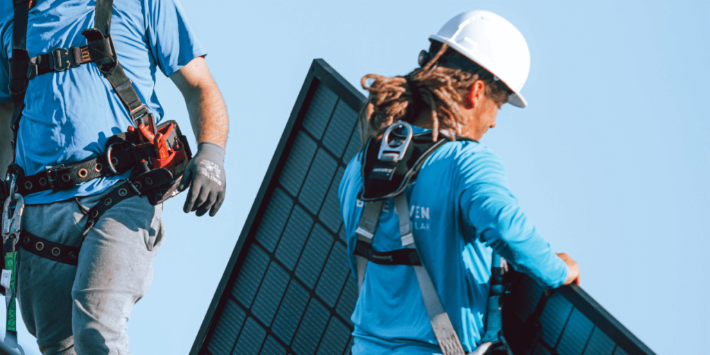 What is the Size of a Solar Panel-02 Blue Raven Solar installer, in safety equipment, carrying a panel on a roof