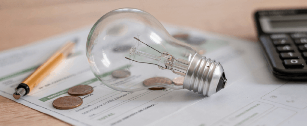 Light bulb sitting on top of paperwork, pennies, with a pen and calculator in the background