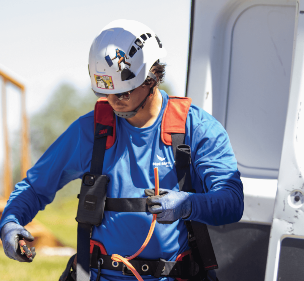 Option_10 Sq Blue Raven Solar installer in a harness and hard hat, retrieving specialized tools from the branded van