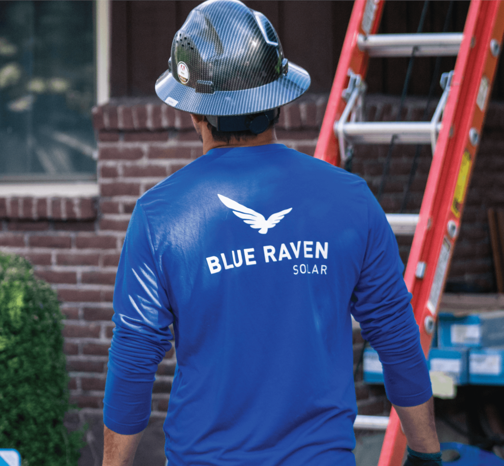 Option_6 Sq Blue Raven Solar installer in a branded blue, long-sleeve shirt with a hard hat approaching a ladder