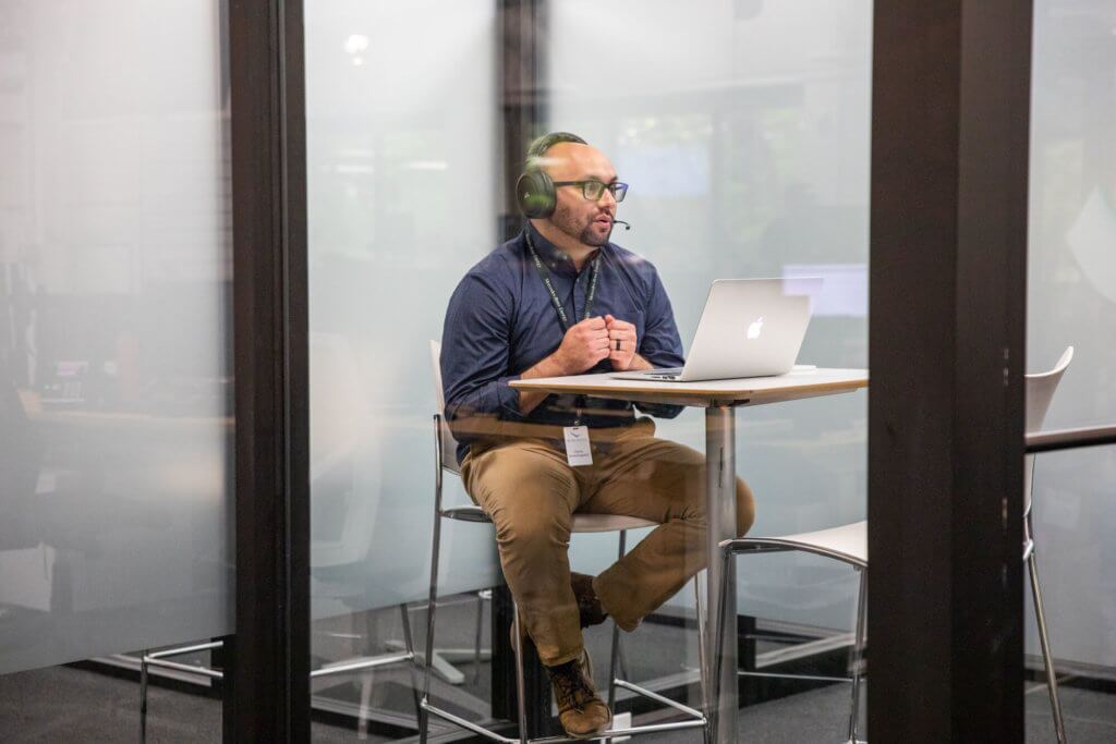 Blue Raven Staged Photos -89 Blue Raven Solar employee in navy blue button up shirt and khaki pants, sitting in a conference room with headset and laptop